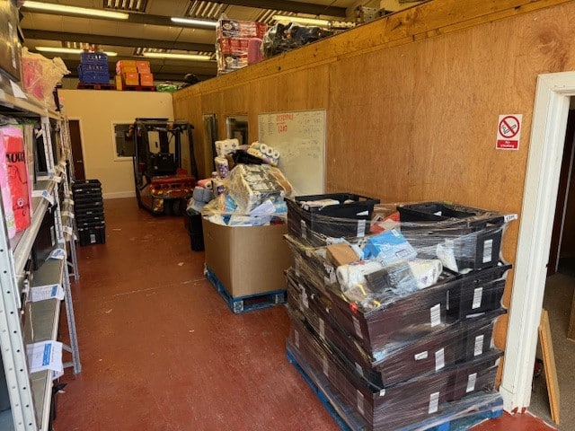 Industrial storage area with wrapped pallets, boxes, and a forklift in the background.